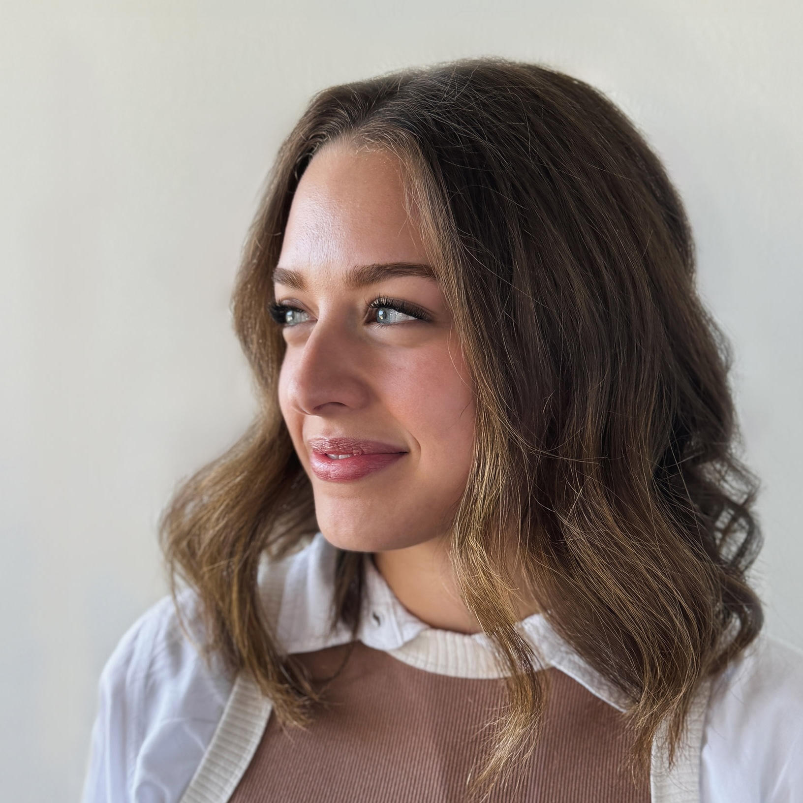 Alexa Urrea's headshot. Young woman with shoulder-length wavy light brown hair looking to the left, wearing a white collared shirt and beige sweater. 