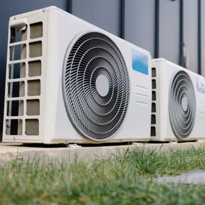 Two outdoor air conditioning units installed on concrete pads beside a building wall above grass.
