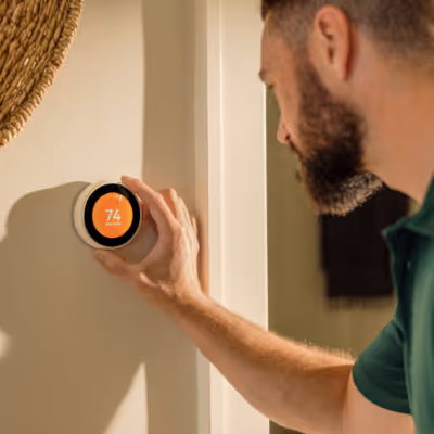 Man adjusting a smart thermostat on a beige wall showing a temperature.