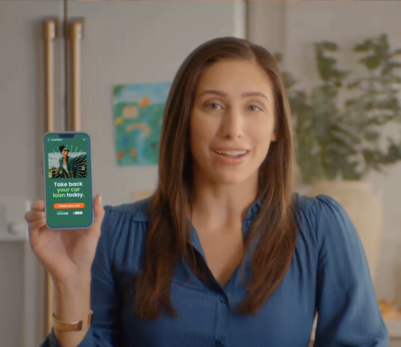 Woman in blue blouse holding phone showing app with text 'Take back your car loan today.'