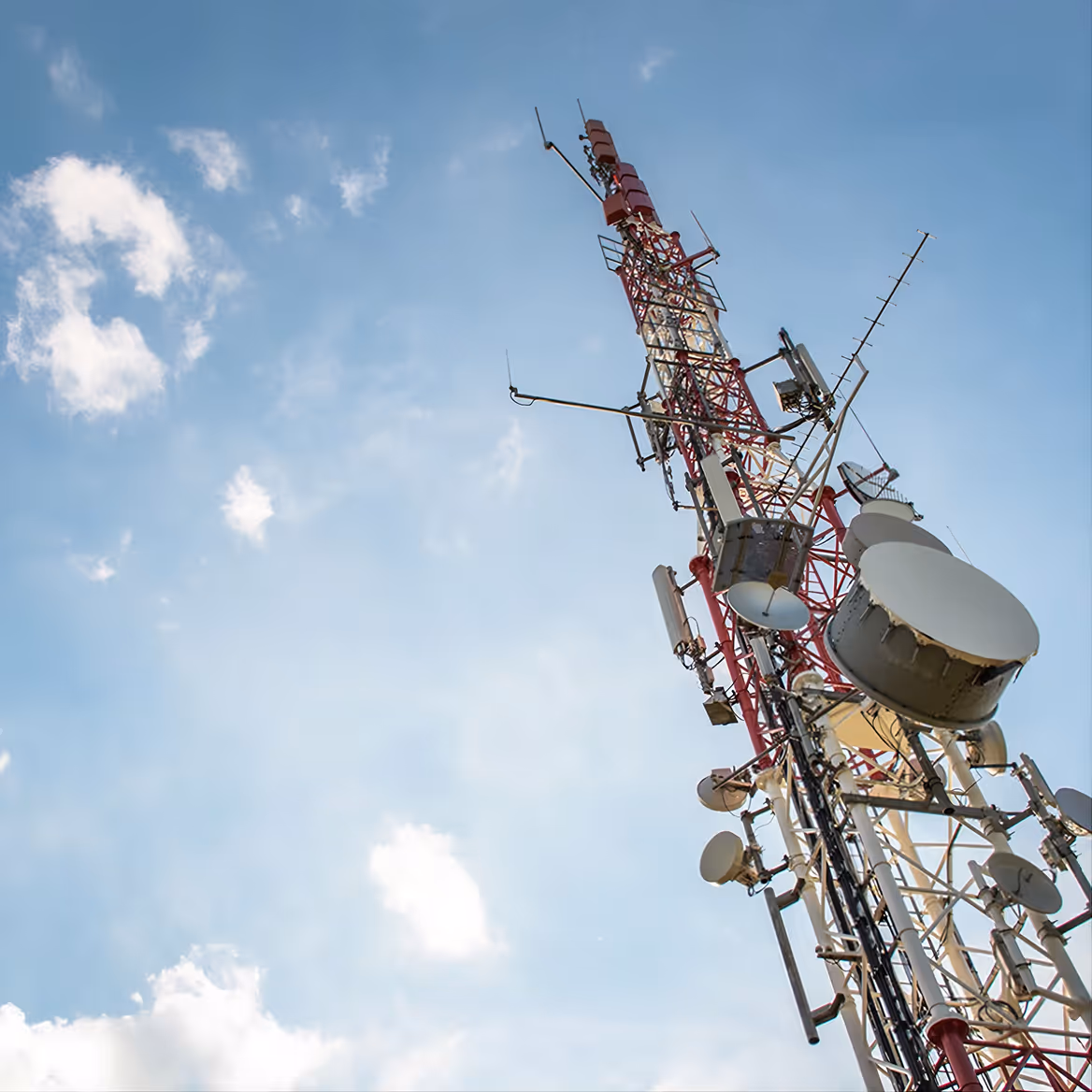 Tall telecommunications tower with multiple antennas against a partly cloudy blue sky.