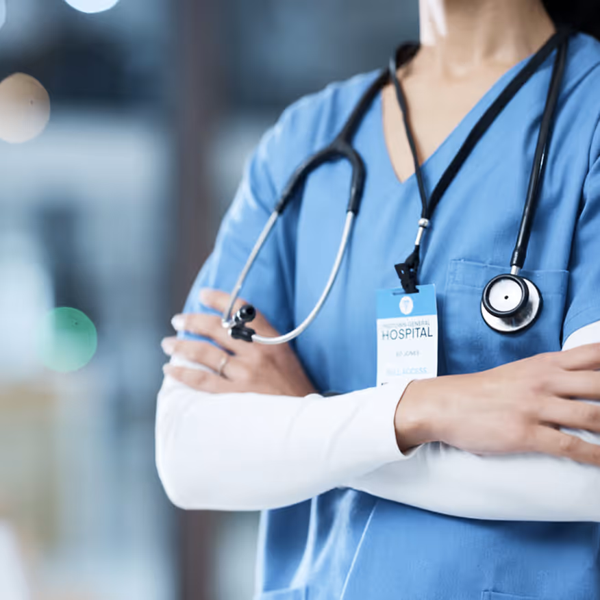 Healthcare professional in blue scrubs with stethoscope with arms crossed.