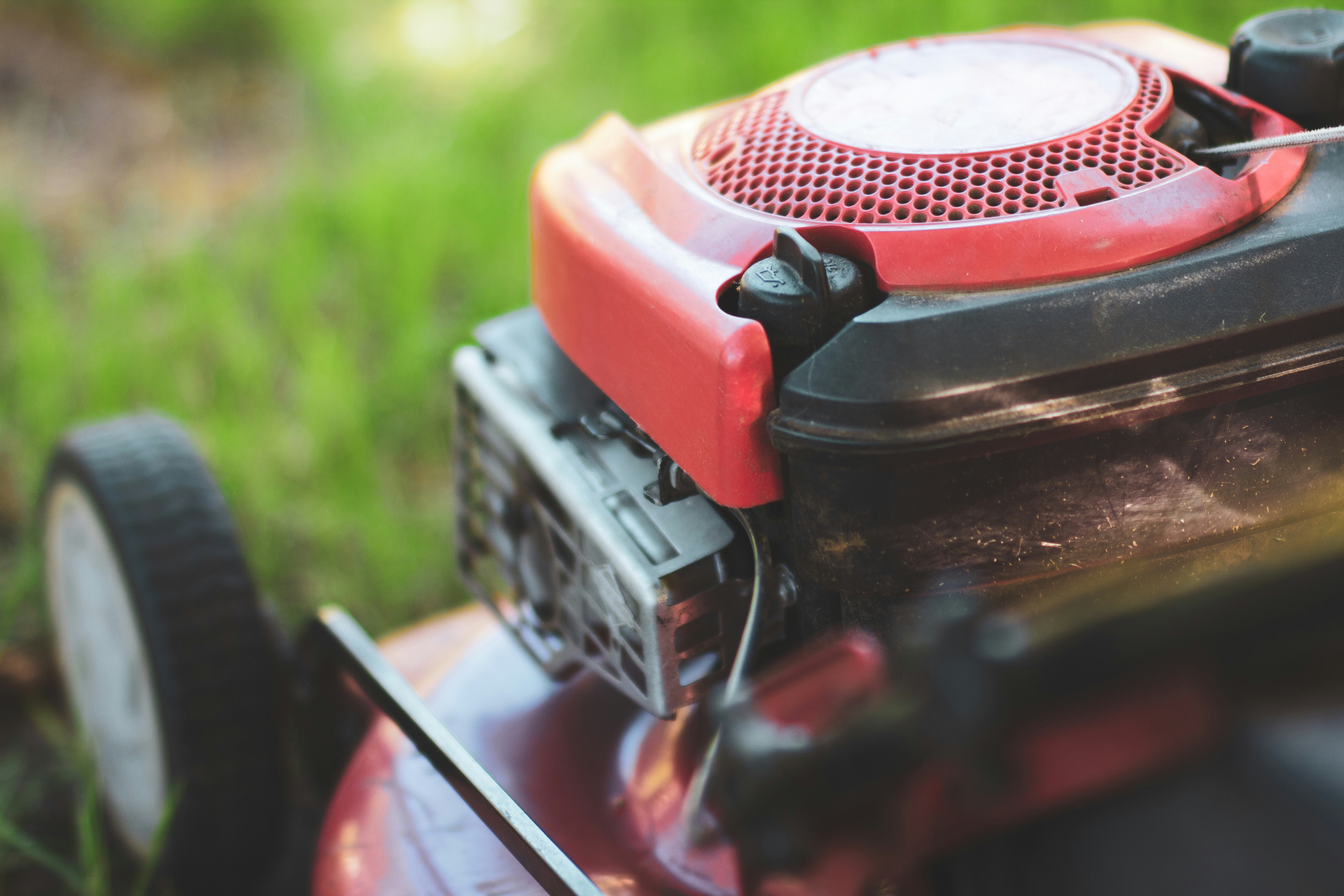 Nahaufnahme Benzinmotor eines roten Rasenmähers auf grünem Rasen