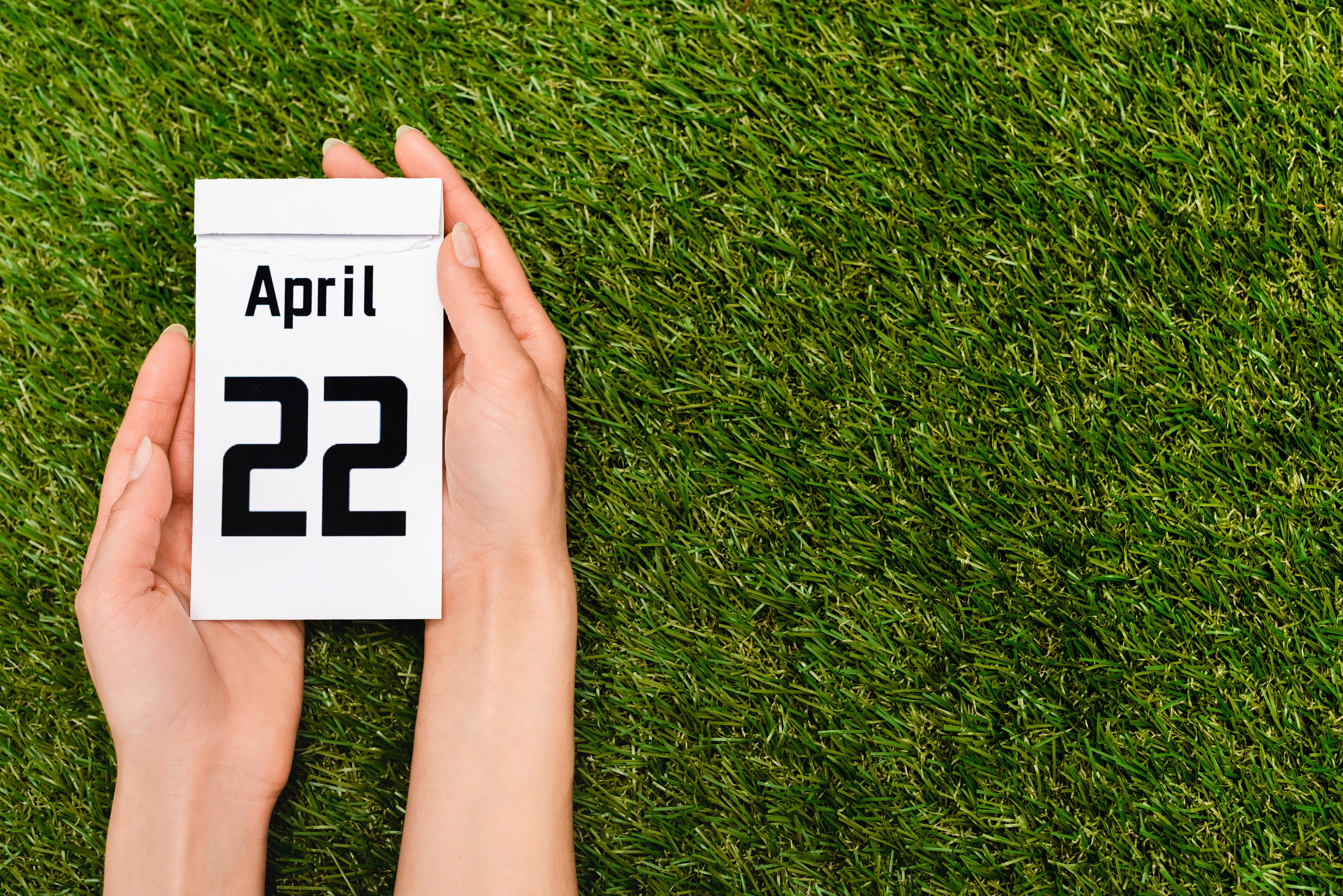 Abreißkalender zeigt 22. April über grünem Rasen – Zeitpunkt für saisonale Rasenpflegemaßnahmen