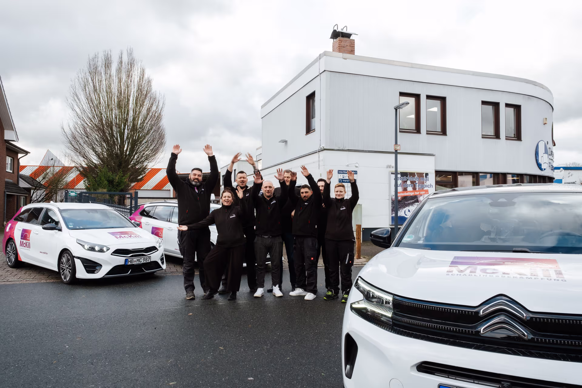 Das McKIll Team neben ihren Firmenfahrzeugen und alle reißen die Arme hoch