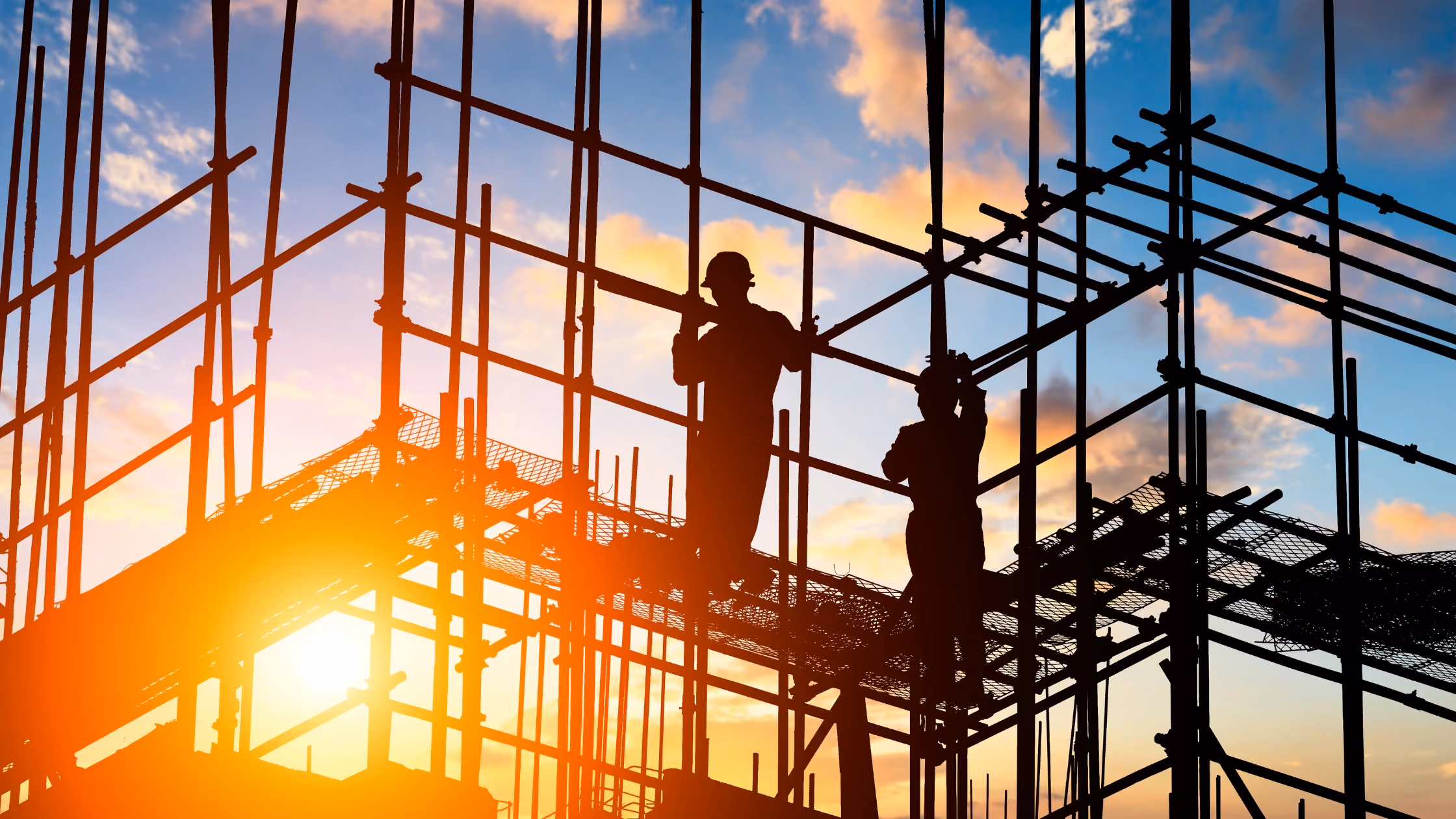 Construction workers silhouetted against a sunset on scaffolding, representing the high-risk environments where verified safety training certification is a matter of life and safety.