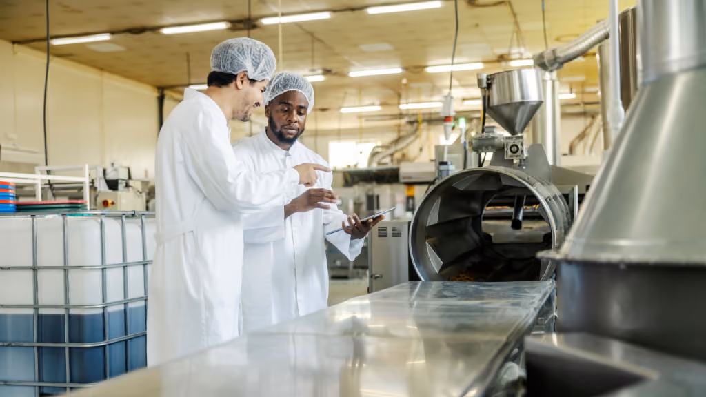 Two workers in factory looking over a tablet while learning on the job.