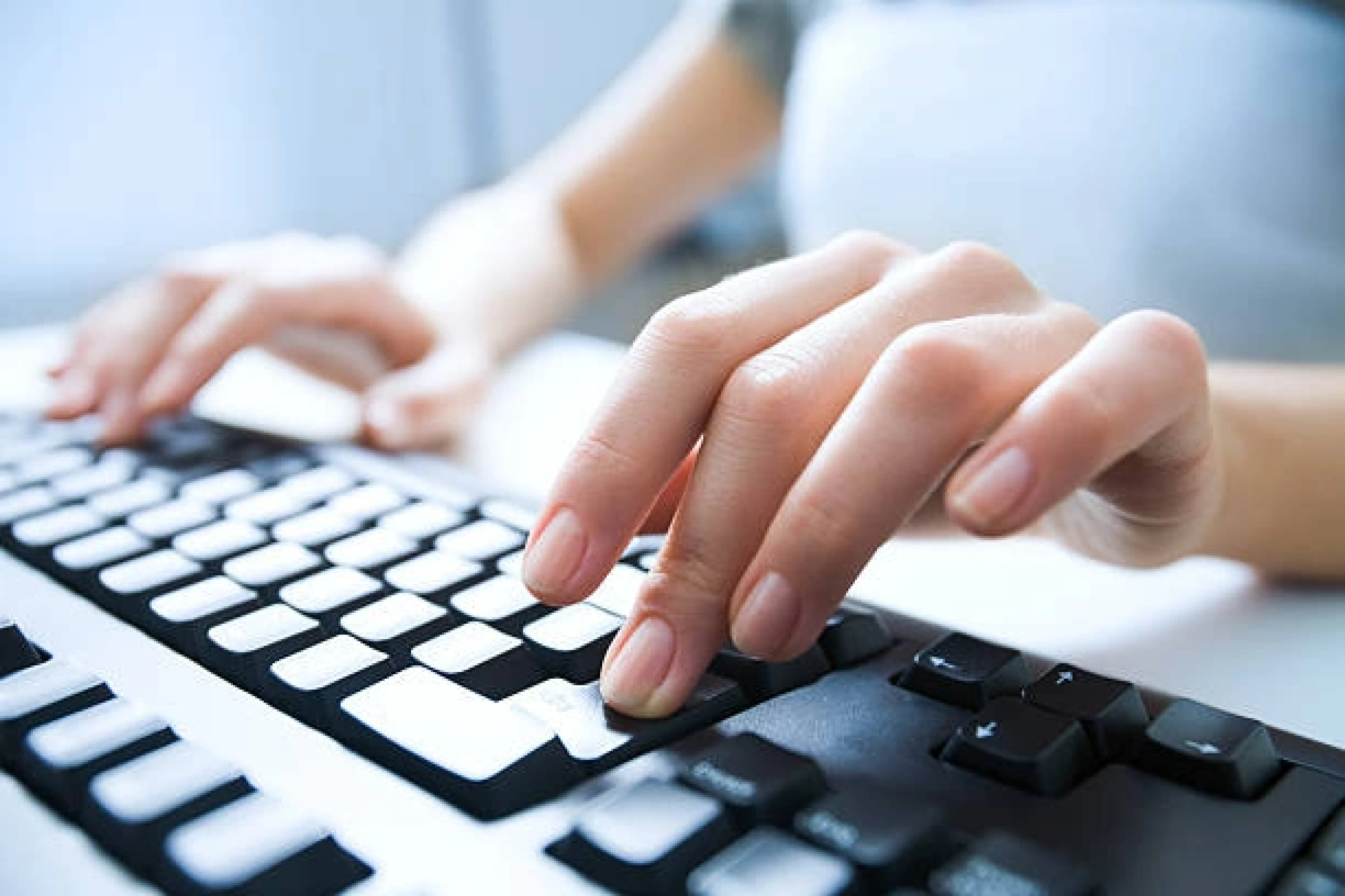 Woman working on a laptop at a home desk, with plants and natural light in the background.
