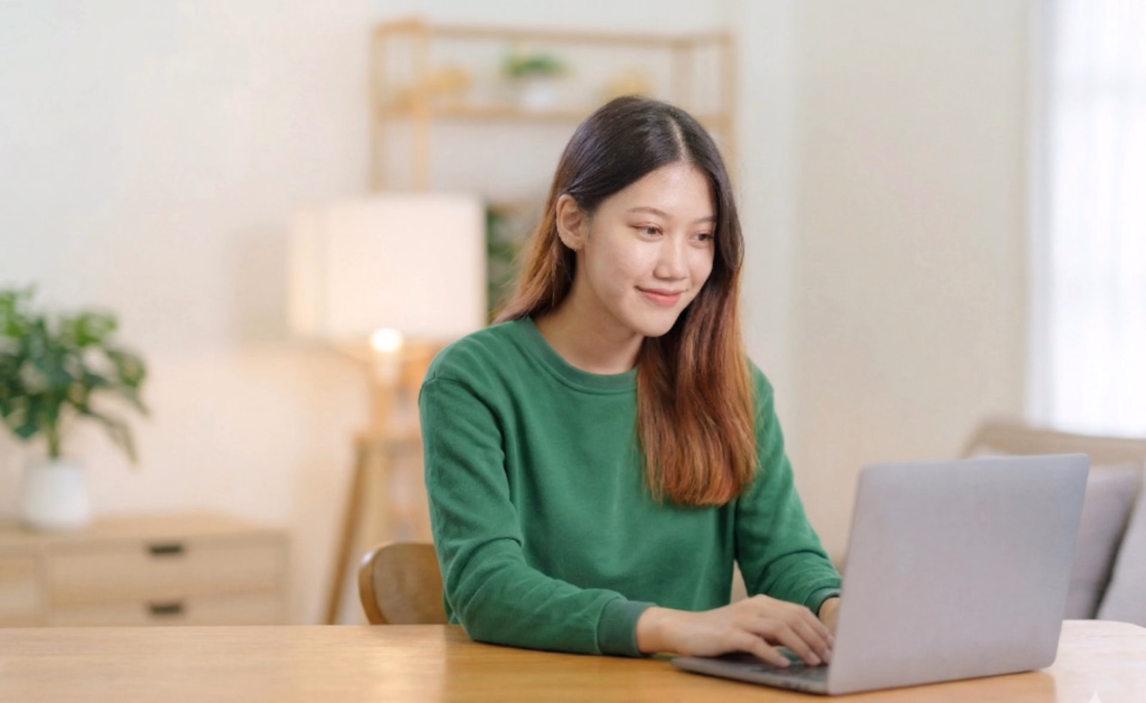 Woman smiling while typing on a laptop at home, representing a comparison guide to the top online proctoring platforms.