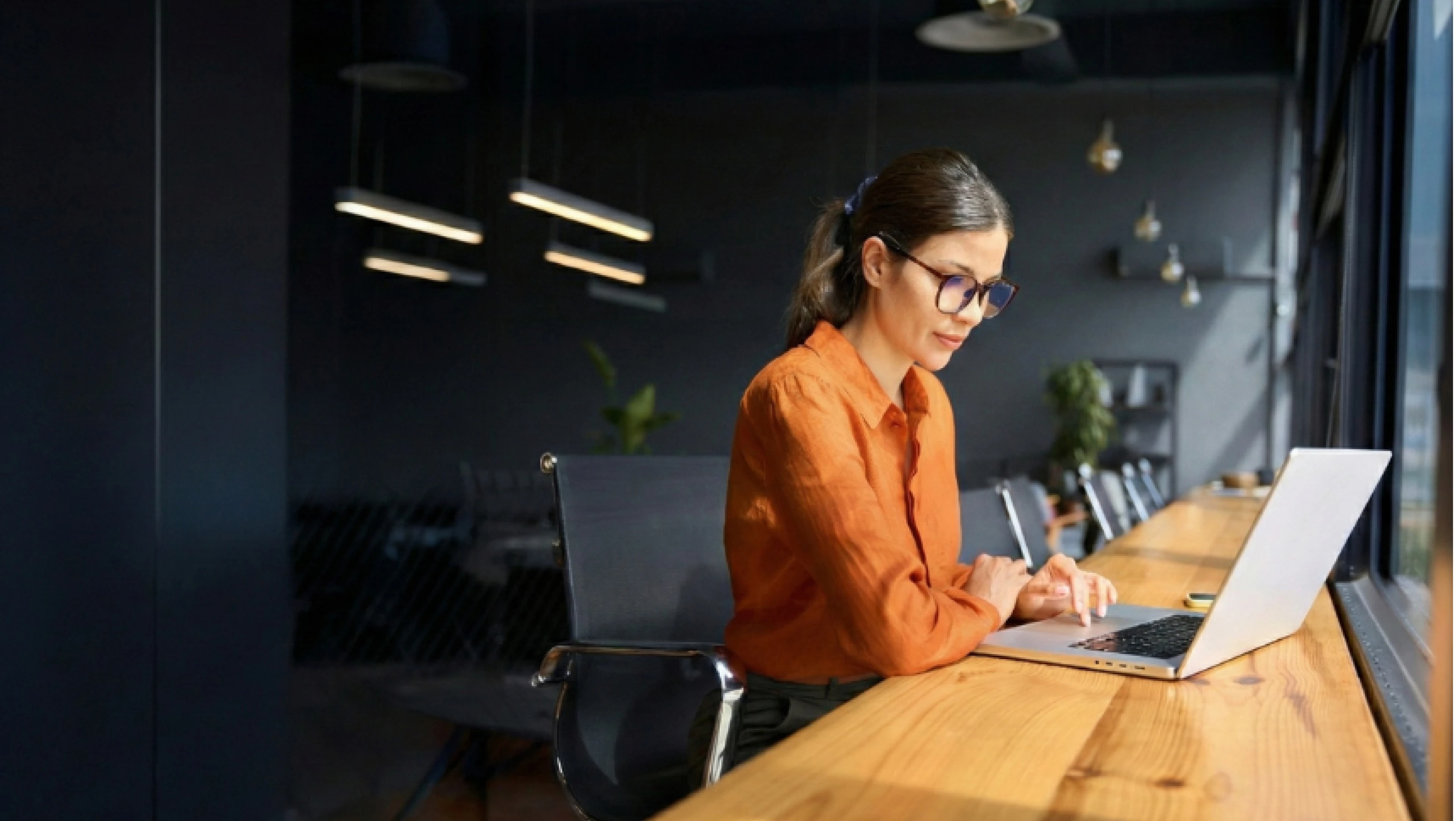 A professional works focused at a laptop in a modern conference room, representing the assessment administrators and program leaders who need a proactive, defensible approach to online proctoring.