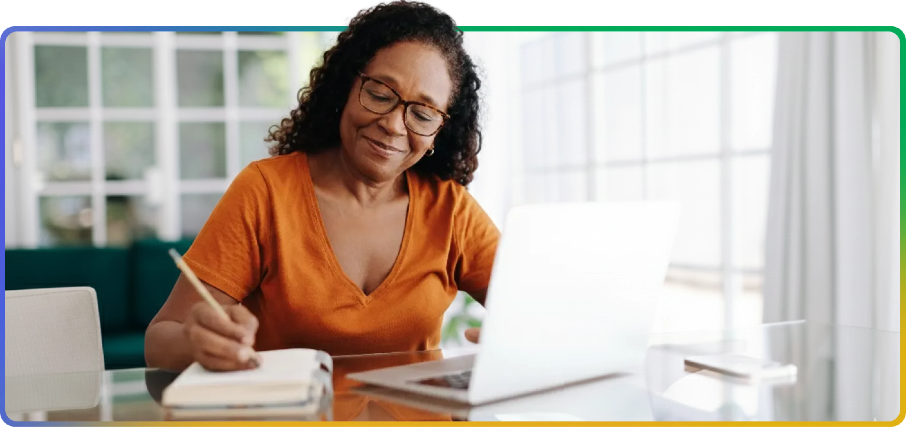 Woman working on a laptop at a home desk, with plants and natural light in the background.