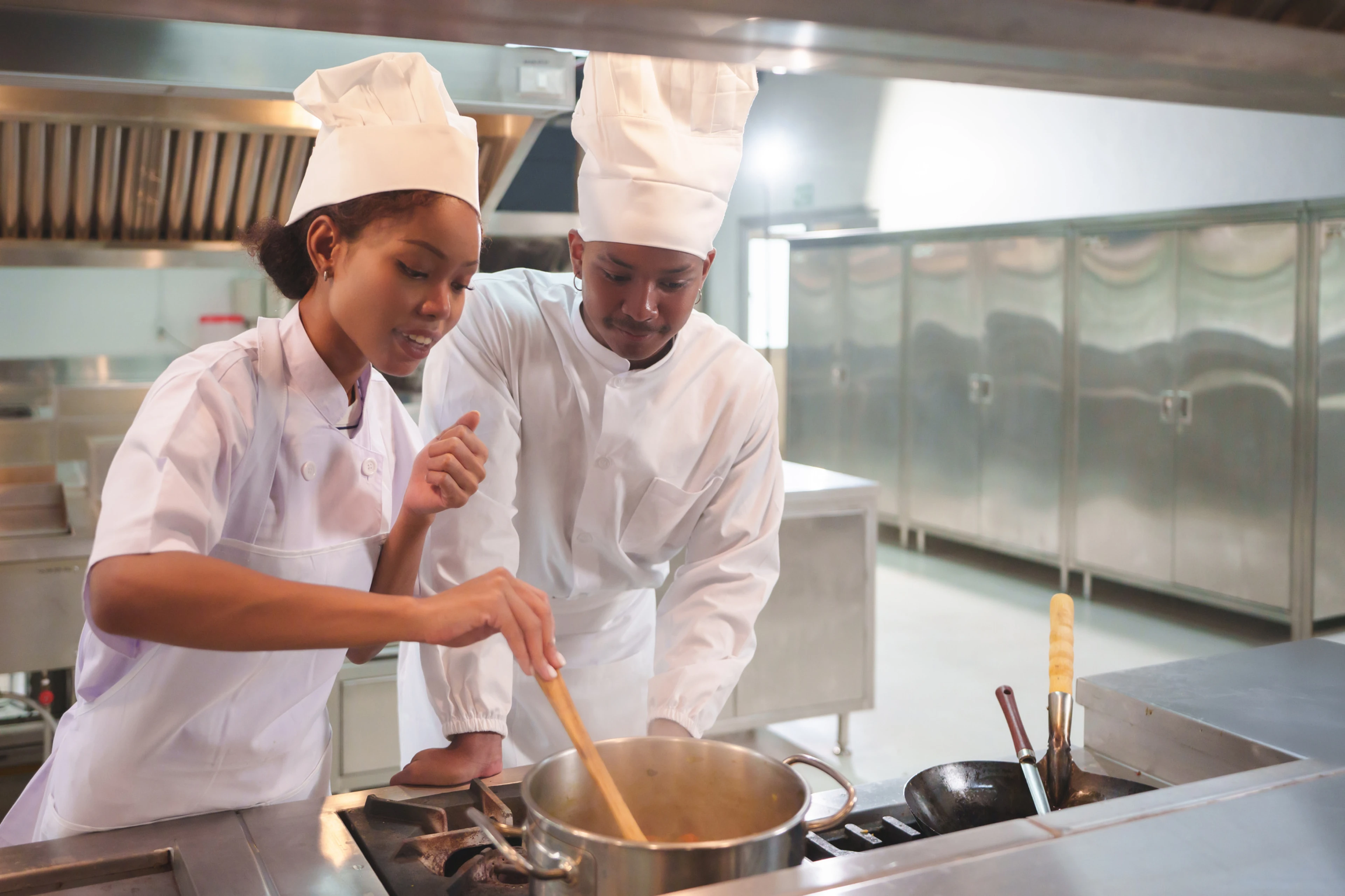 Two chefs in white uniforms work together at a stove in a professional kitchen, representing food service staff pursuing ANSI-CFP accredited certification.