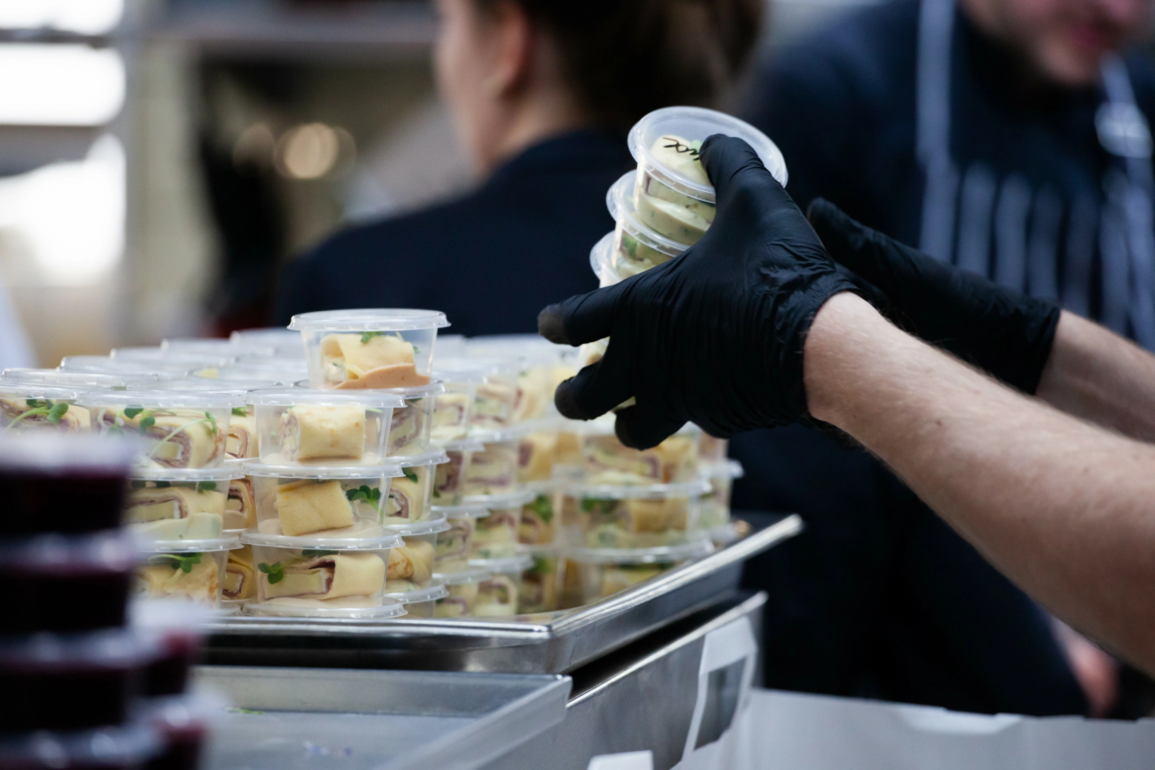 A food service worker in gloves packages prepared food in a commercial kitchen, representing a food handler pursuing proctored food safety certification.