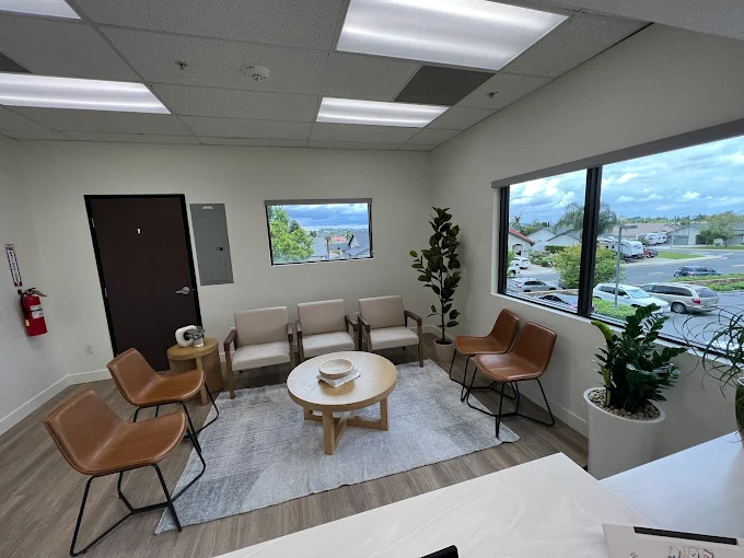 Bright waiting room at CL Family Dentistry in La Verne with neutral chairs, a round wood coffee table, and large windows overlooking the neighborhood