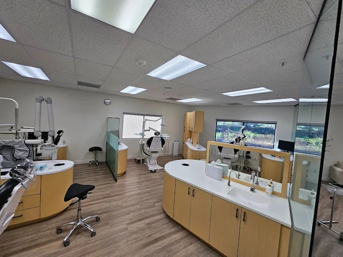 Open dental operatory at CL Family Dentistry featuring two patient chairs, overhead lighting, prep counter with sink, and a window with a hillside view