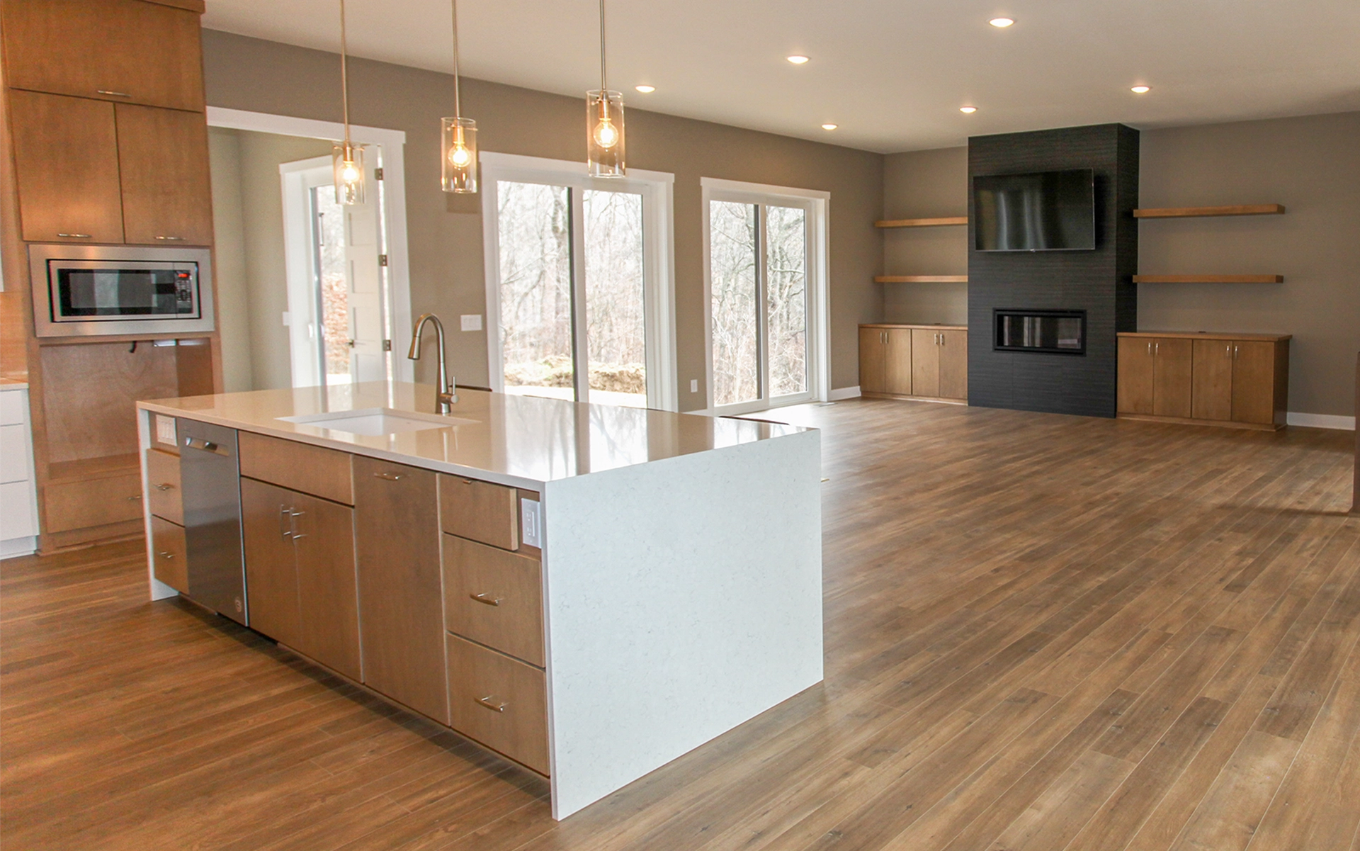 Open living room and kitchen with wood floors, large island, windows, and a fireplace with TV above.