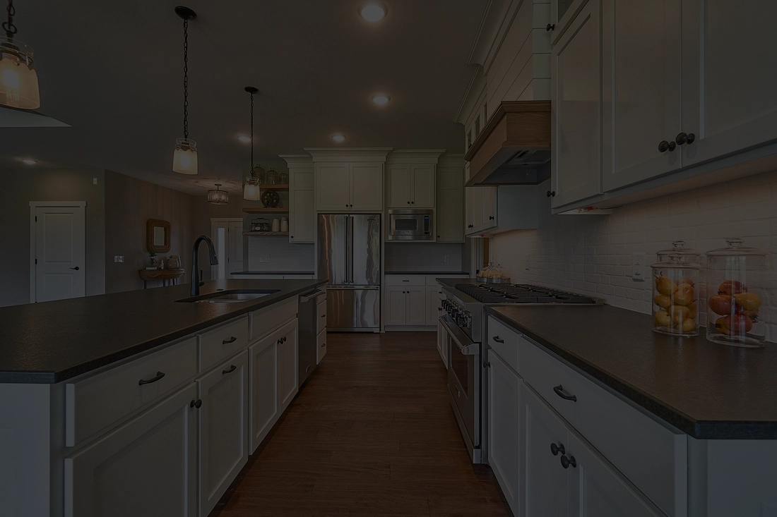 Modern kitchen with white cabinets, stainless steel appliances, dark countertops, and wooden floor.