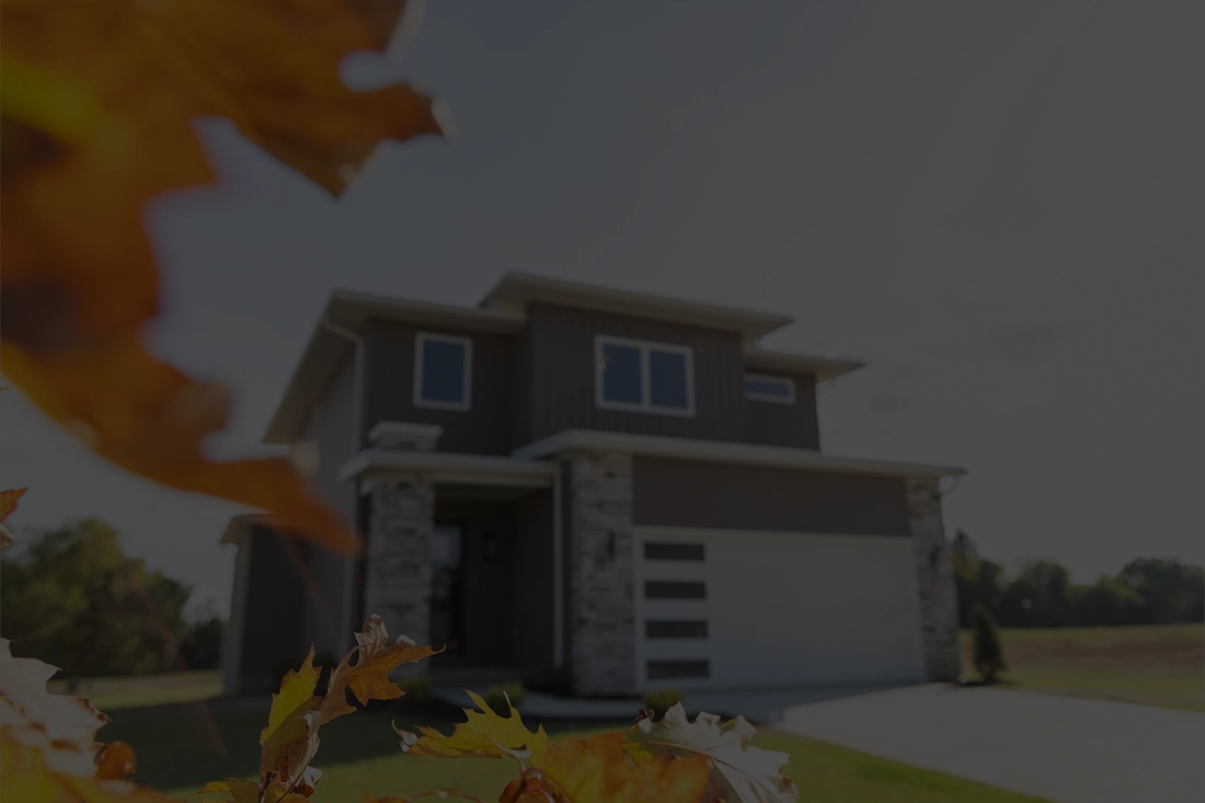 Modern two-story house with stone accents and a white garage door in a grassy area with autumn leaves.