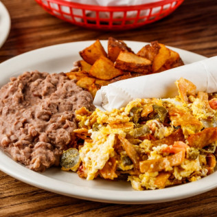 Plate with scrambled eggs mixed with vegetables, a serving of refried beans, and roasted potato wedges.