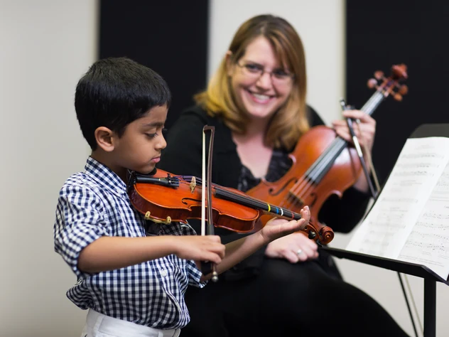 Young boy playing violin beside his teacher during a lesson in Powell, Ohio