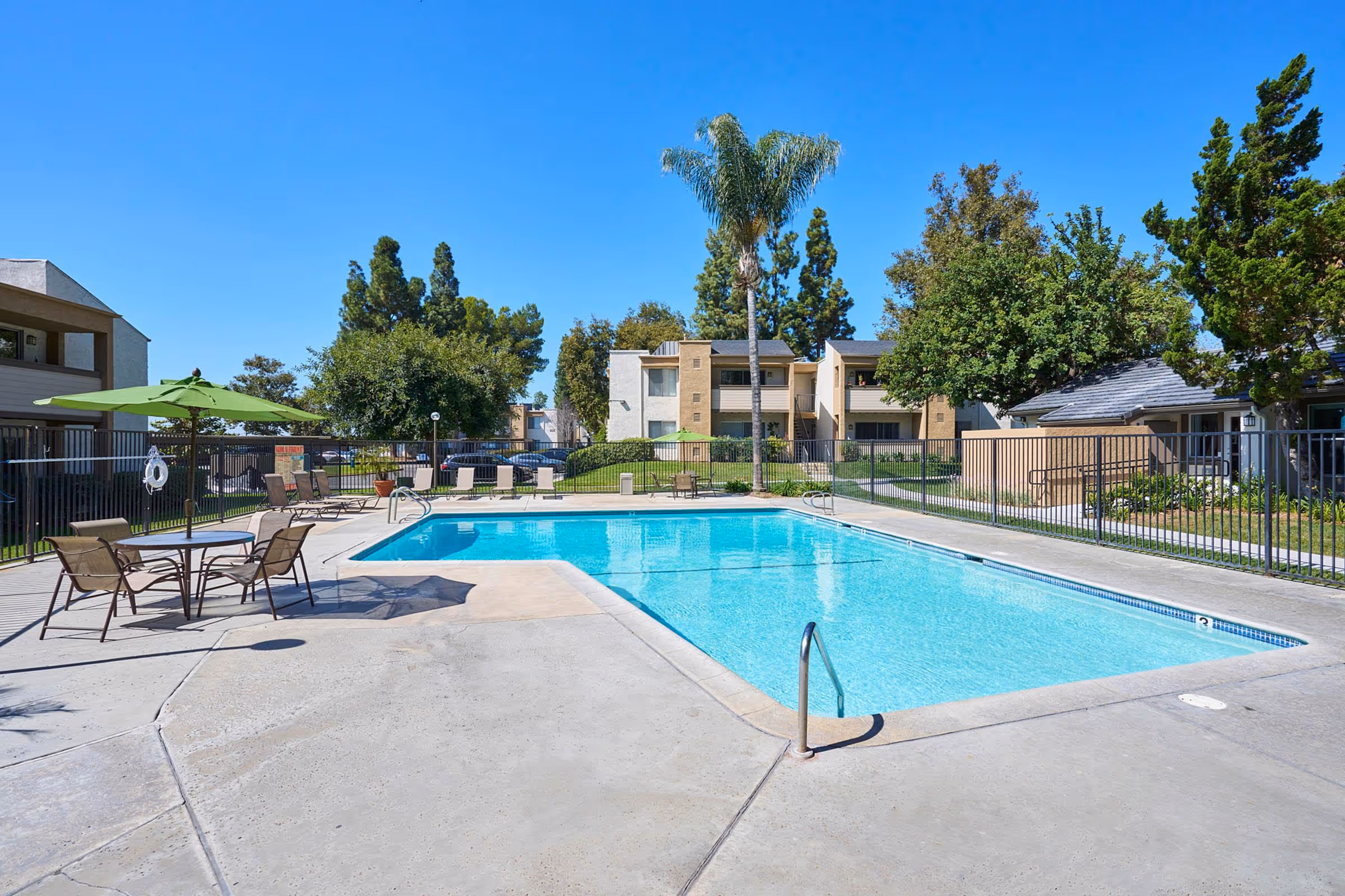 Swimming pool with view of exterior, lounge chairs, and table and chairs with umbrellas 