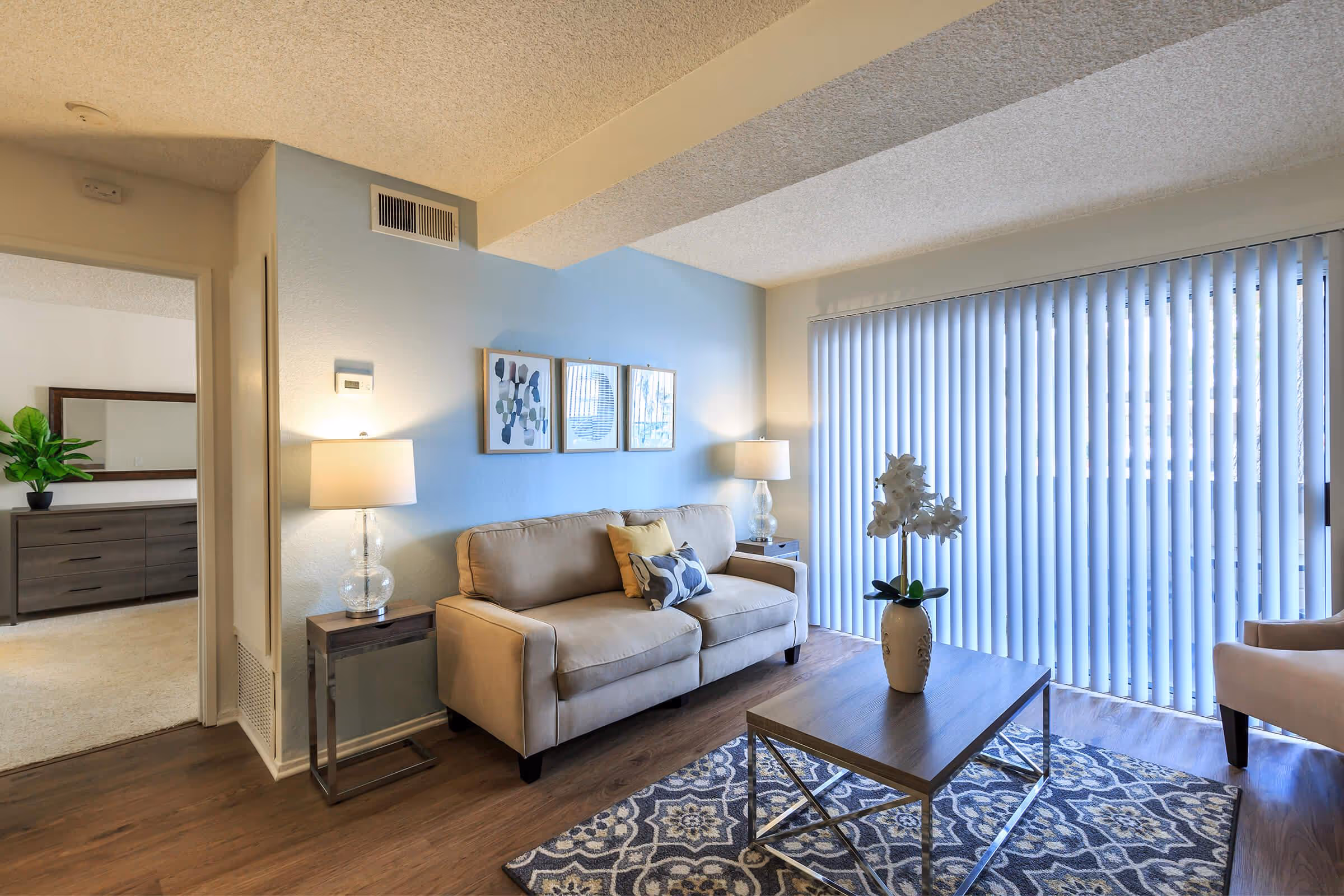 Wide view of living area featuring sofa, coffee table, and sliding doors to balcony with view into bedroom