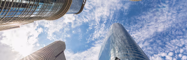 Upward view of modern glass skyscrapers under a cloudy blue sky.