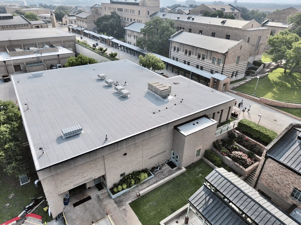 Aerial view of a large building with HVAC units on the roof and surrounding campus pathways and greenery.