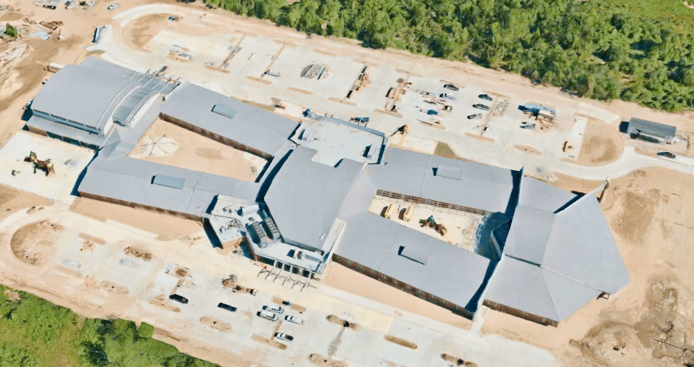 Aerial view of a large building under construction surrounded by dirt and trees.