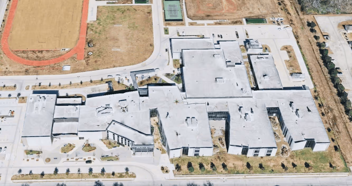 Aerial view of a large school building complex with adjacent sports fields and a running track.