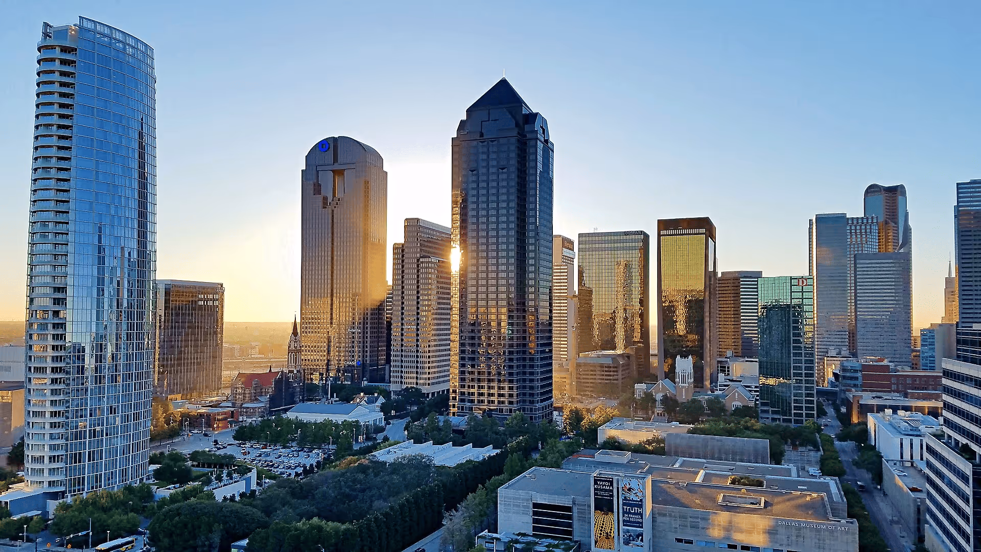 Downtown Dallas skyline at sunset with prominent tall buildings and Dallas Museum of Art in foreground.