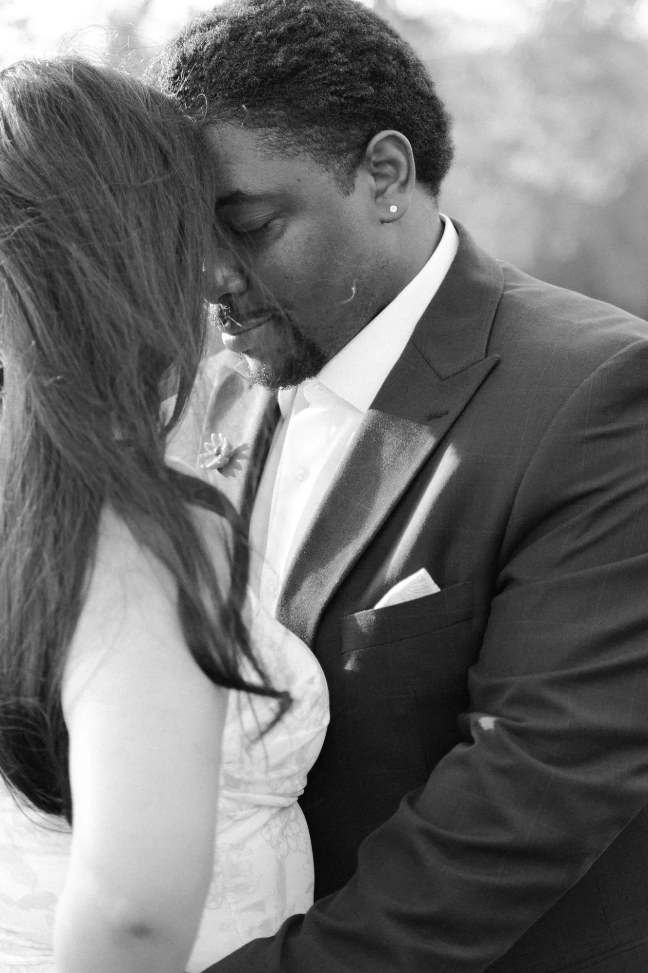 Black and white close-up of a couple in wedding attire with foreheads gently touching, eyes closed, sharing a tender moment.