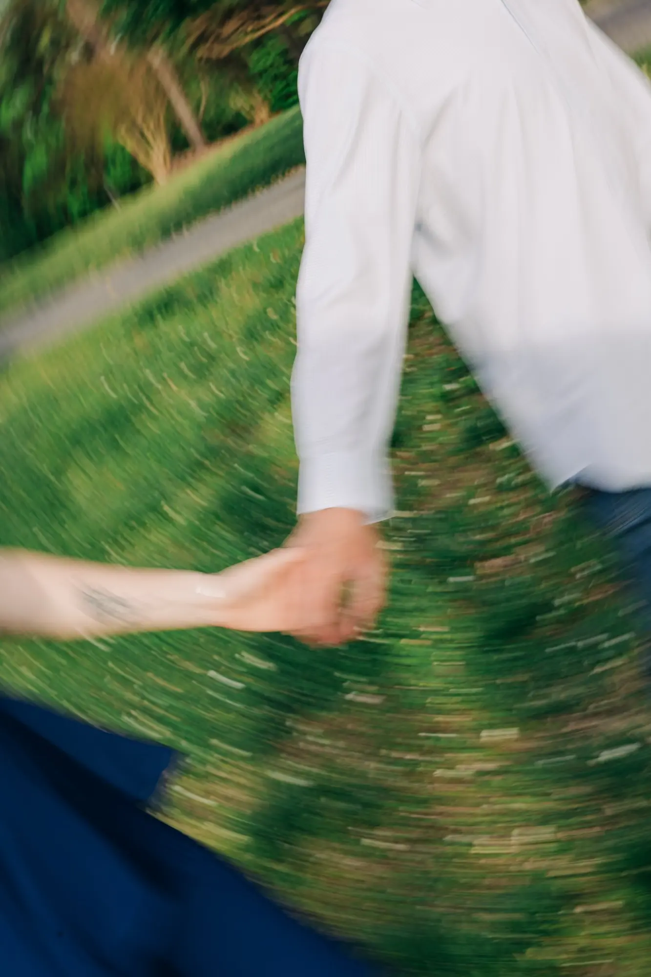 Blurred photo showing two people holding hands outdoors with green grass and trees in the background.