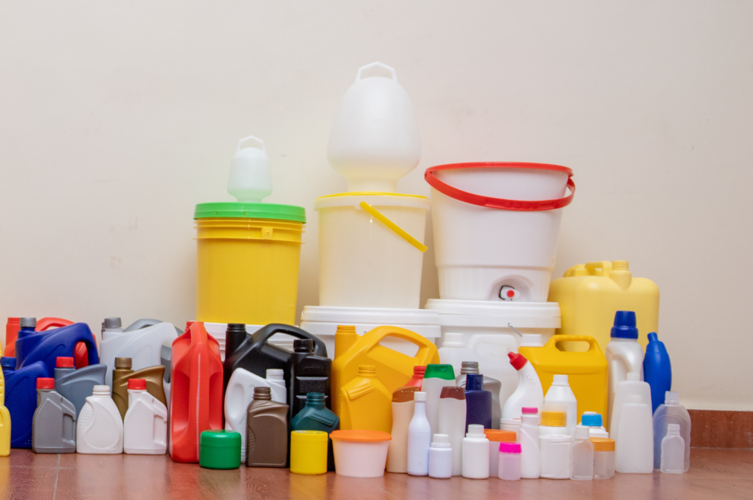 An assortment of colorful HDPE plastic containers — jerricans, jugs, buckets, pails and bottles in blue, yellow, red, white and black — arranged together on a wood floor.