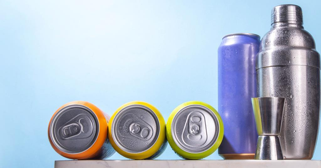 Colorful aluminum beverage cans lying and standing beside a stainless steel cocktail shaker and jigger against a light blue background.