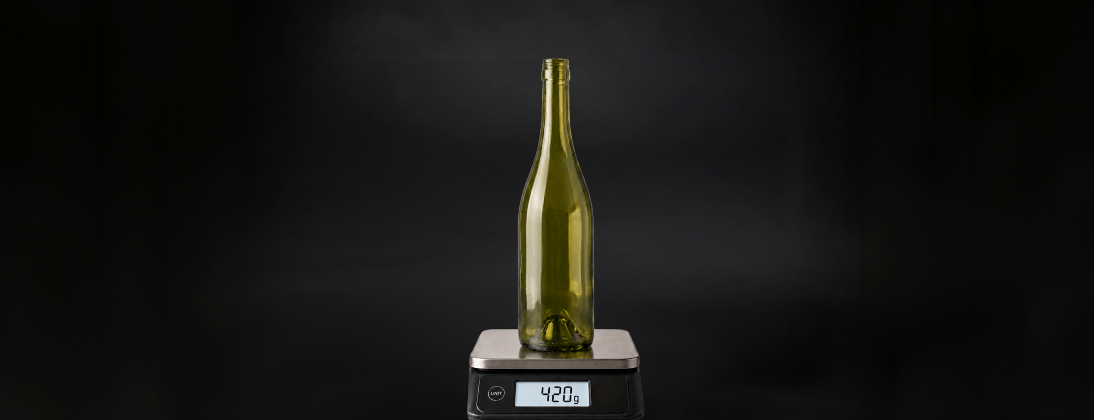 A lightweight antique green glass wine bottle standing on a digital kitchen scale reading 420 g against a black background.