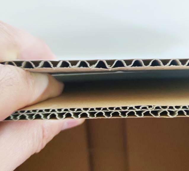Cut edge of corrugated fiberboard showing the wavy fluted medium between flat linerboard sheets.