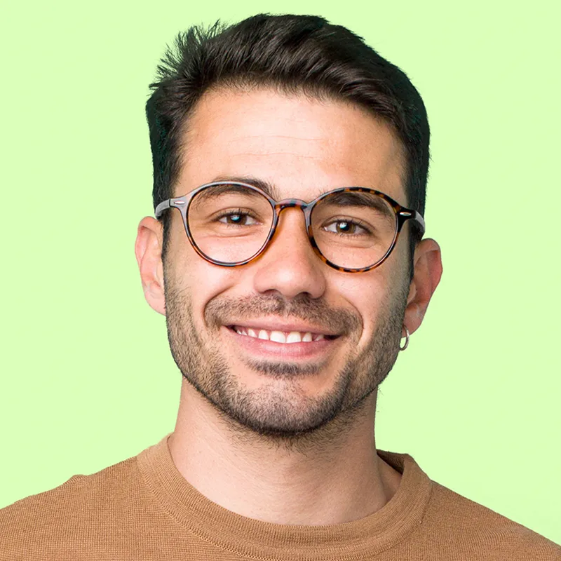 Smiling man with dark hair, tortoiseshell glasses, and an earring against a light green background.