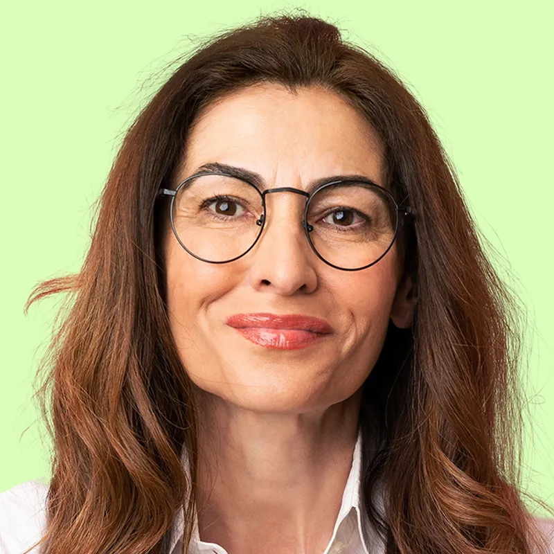 Middle-aged woman with long brown hair, round glasses, and a slight smile, against a light green background.