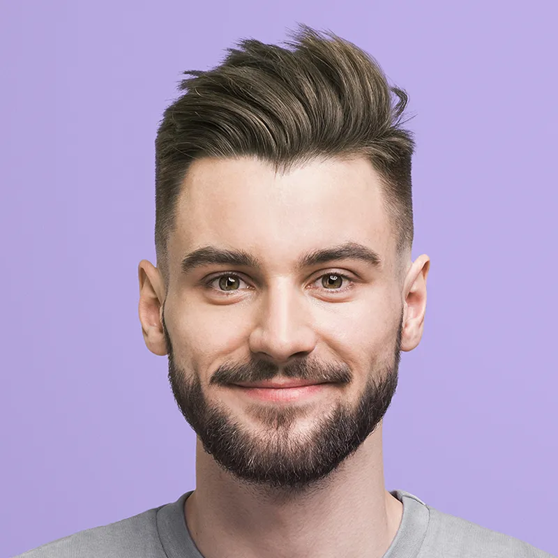 Smiling young man with styled brown hair and beard wearing a gray shirt on a purple background.