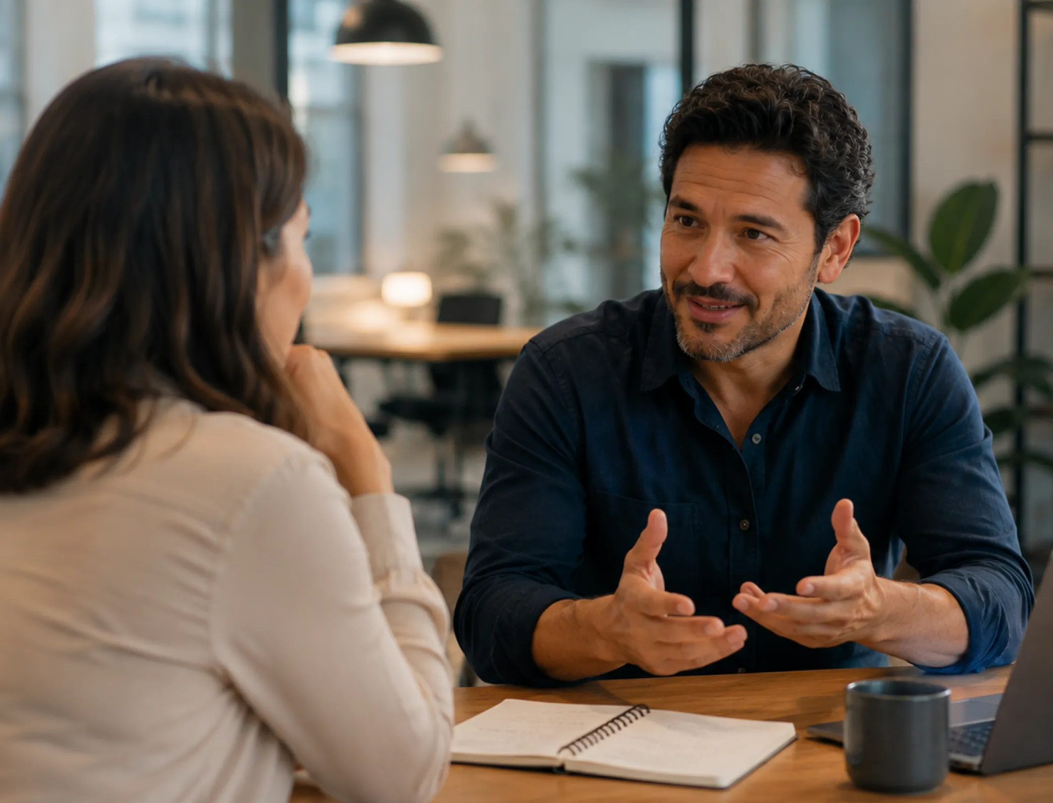 Two colleagues having a discussion in an office with a notebook and coffee mug on the table.