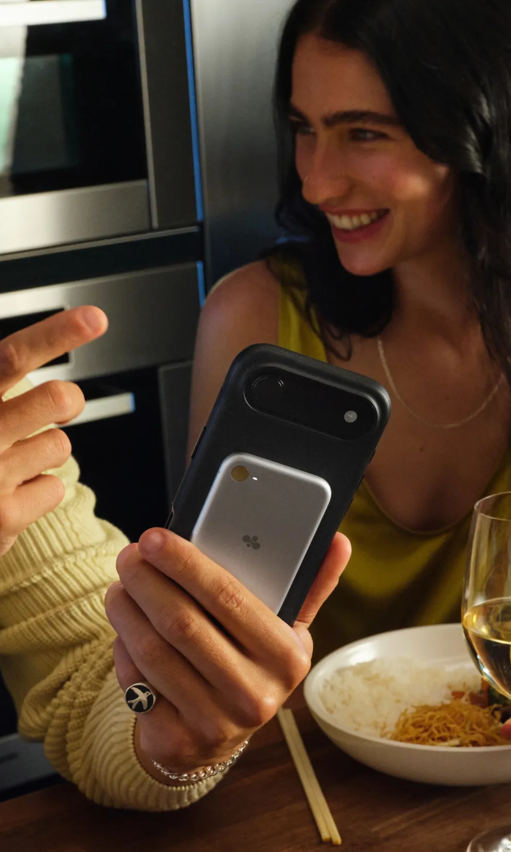Two people smiling at a phone with Bee over dinner