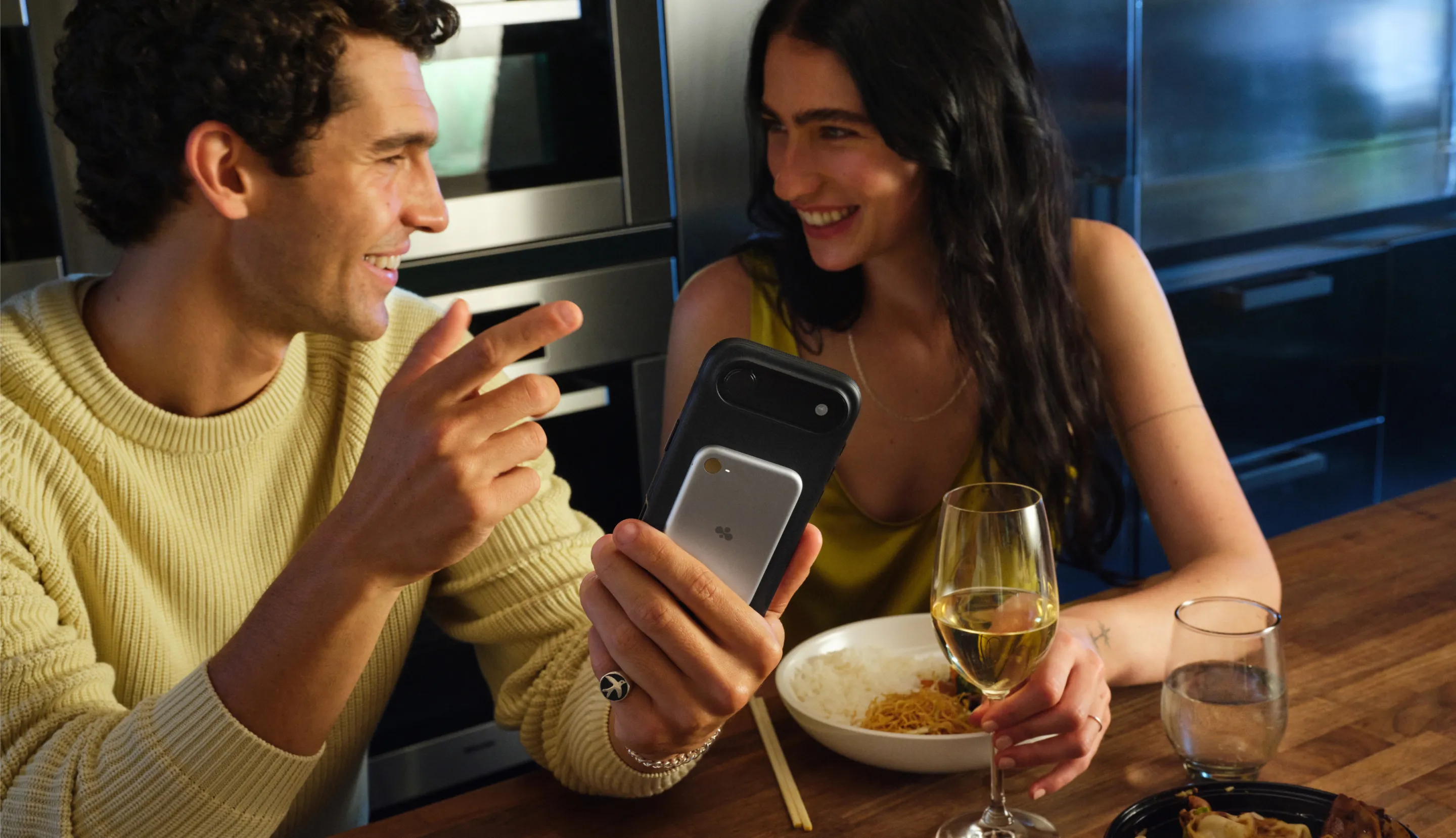 Two people smiling at a phone with Bee over dinner
