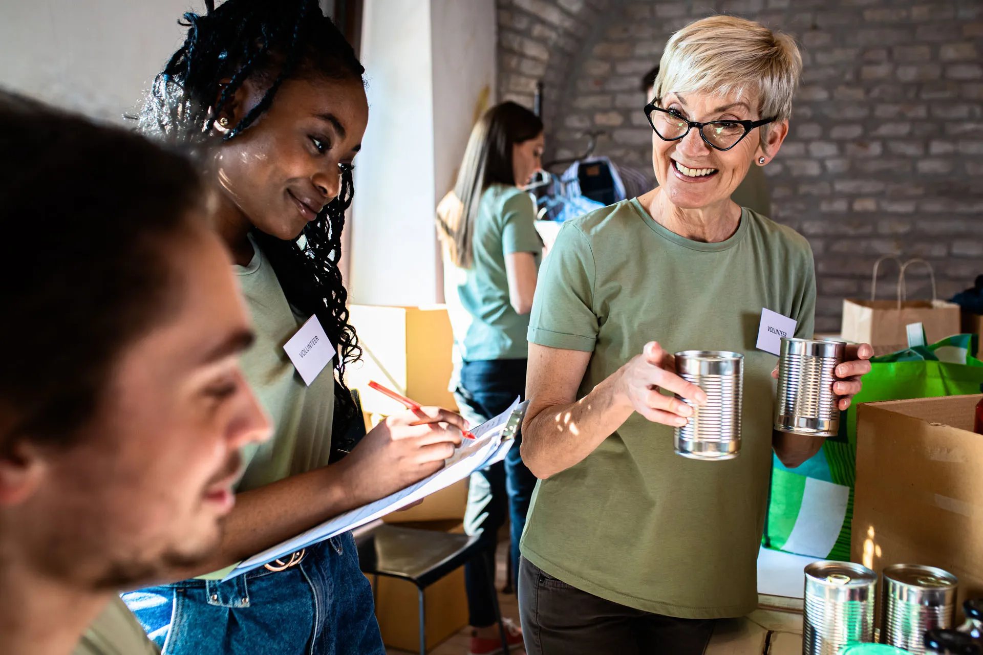 Smiling volunteers sorting canned goods and taking notes during a community charity event.