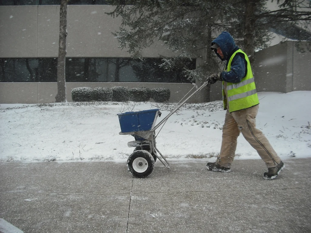worker pushing ice melt spreader