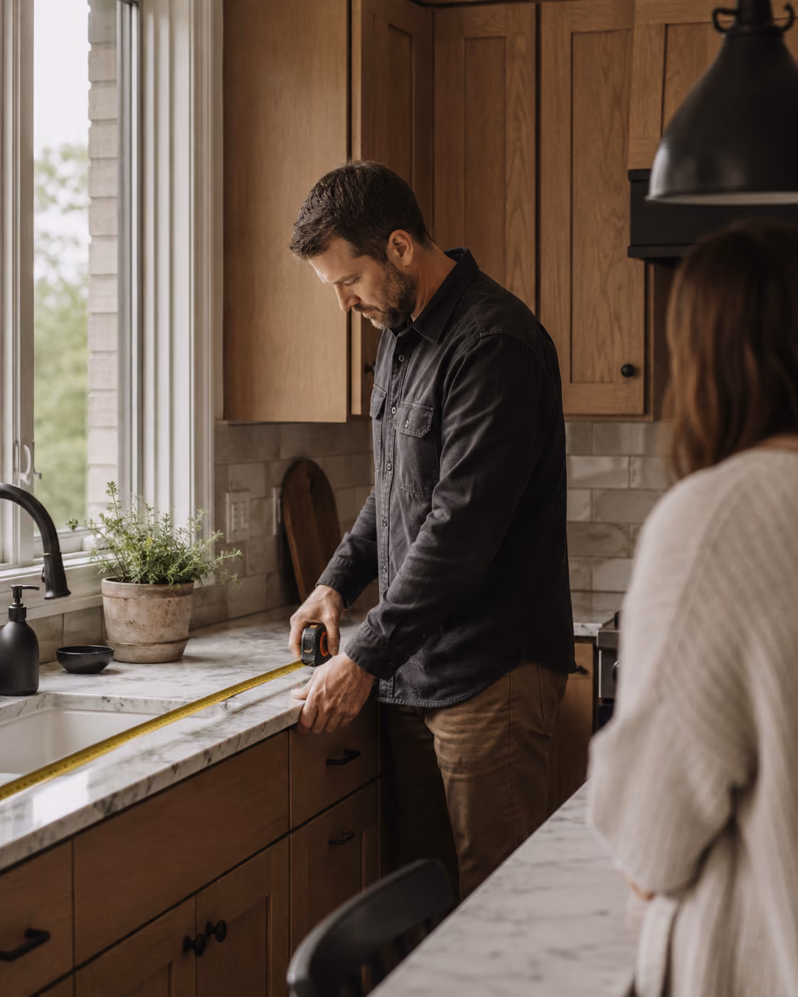 Craftsman measuring a stone kitchen countertop beside a homeowner during an in-home kitchen remodeling consultation.