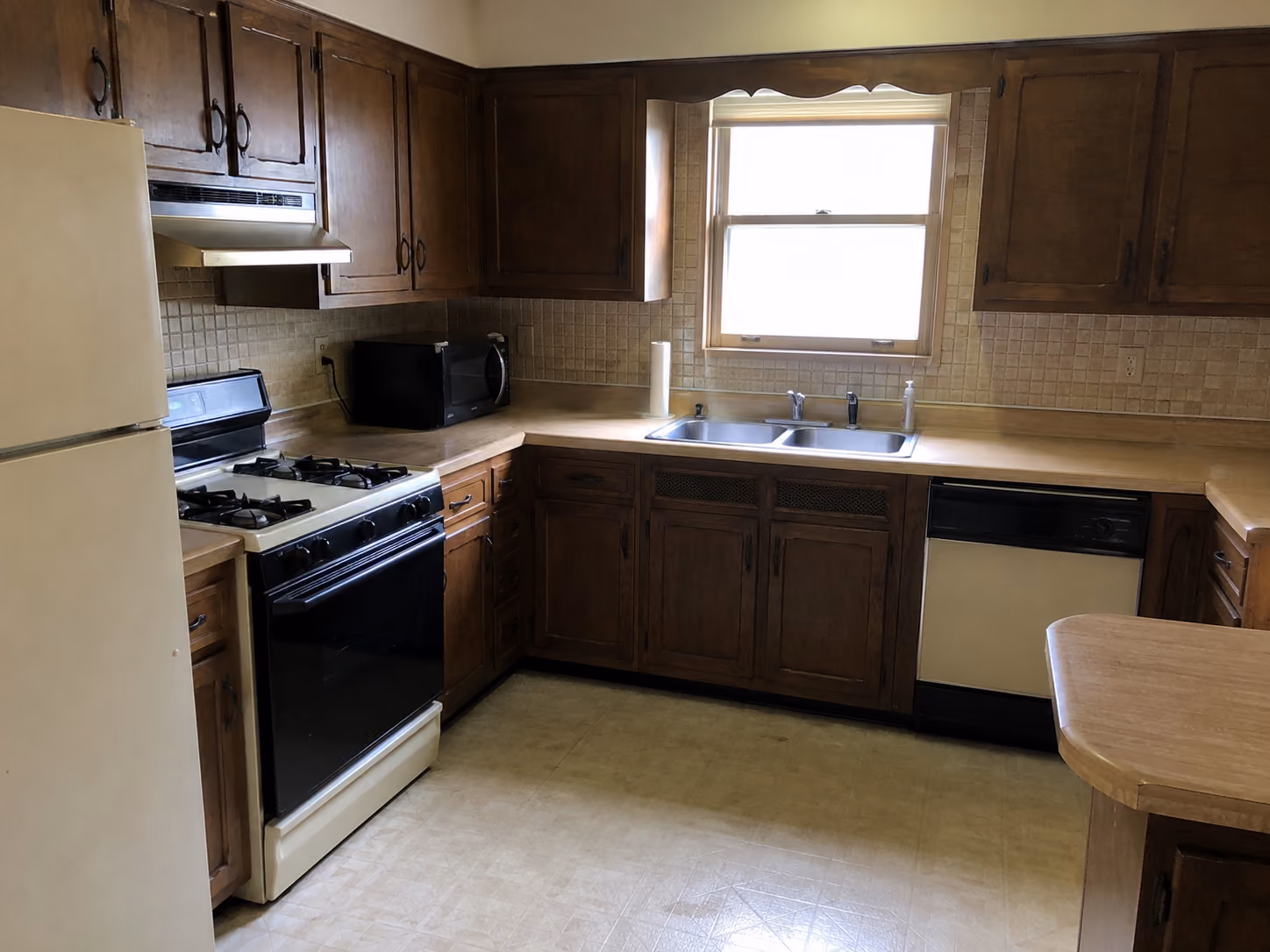 Dated kitchen with dark oak cabinets, laminate countertops, older appliances, and worn vinyl flooring before remodeling.