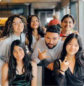 Group of six young adults smiling and posing together indoors.
