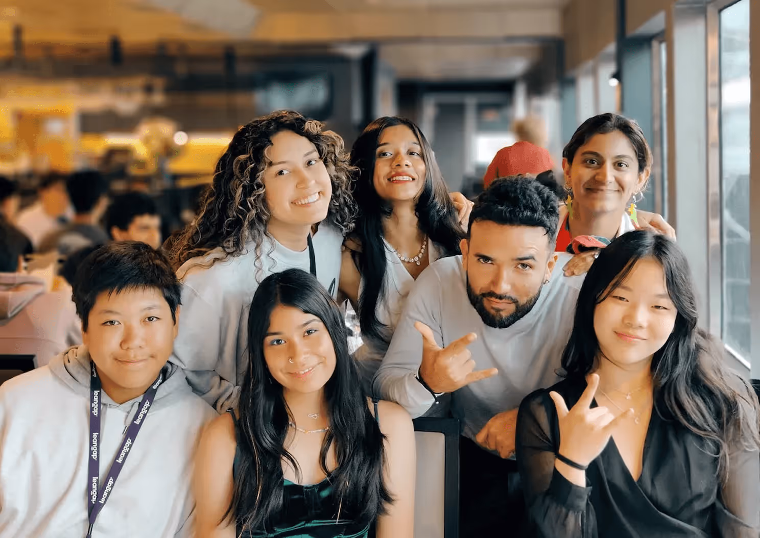 Group of young mentors and students smiling brightly indoors with casual attire and hand gestures.