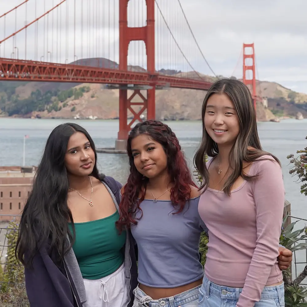 Three teenage students posing together in front of the Golden Gate Bridge